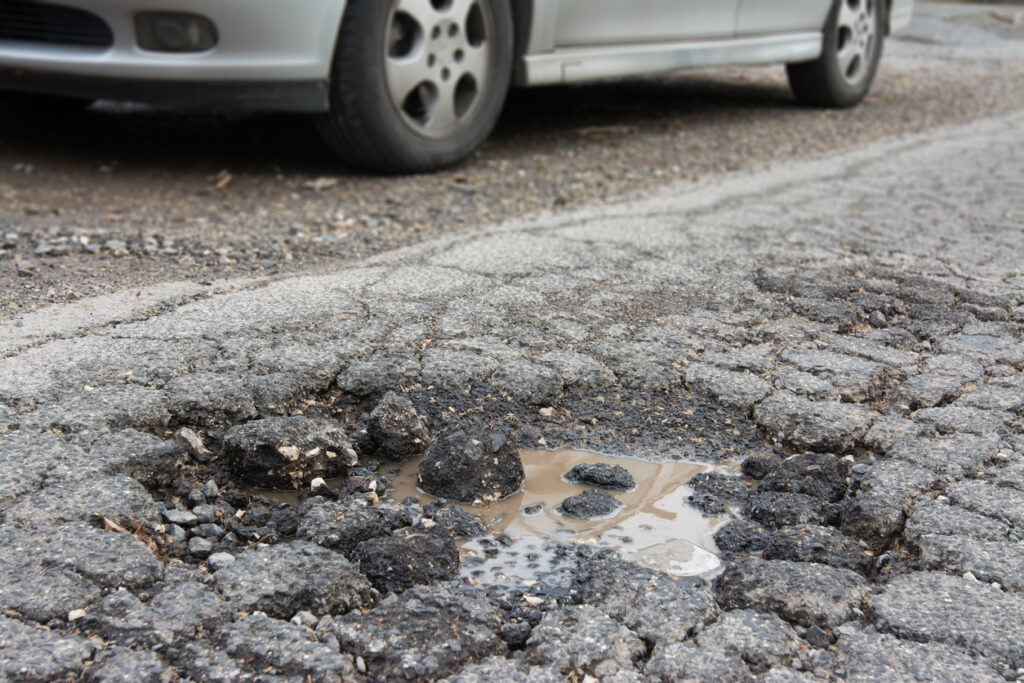 Effects of poor pavement conditions - A car passing through a damaged pavement.
