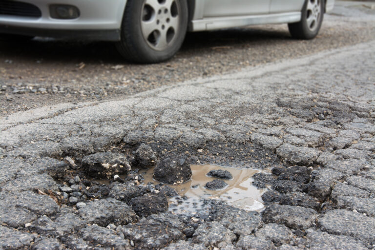 Effects of poor pavement conditions - A car passing through a damaged pavement.