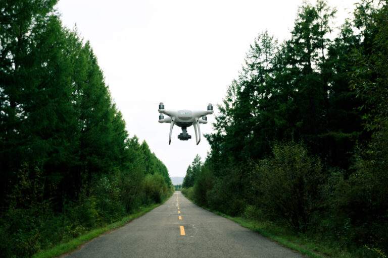 White drone flying over a road in a forest.