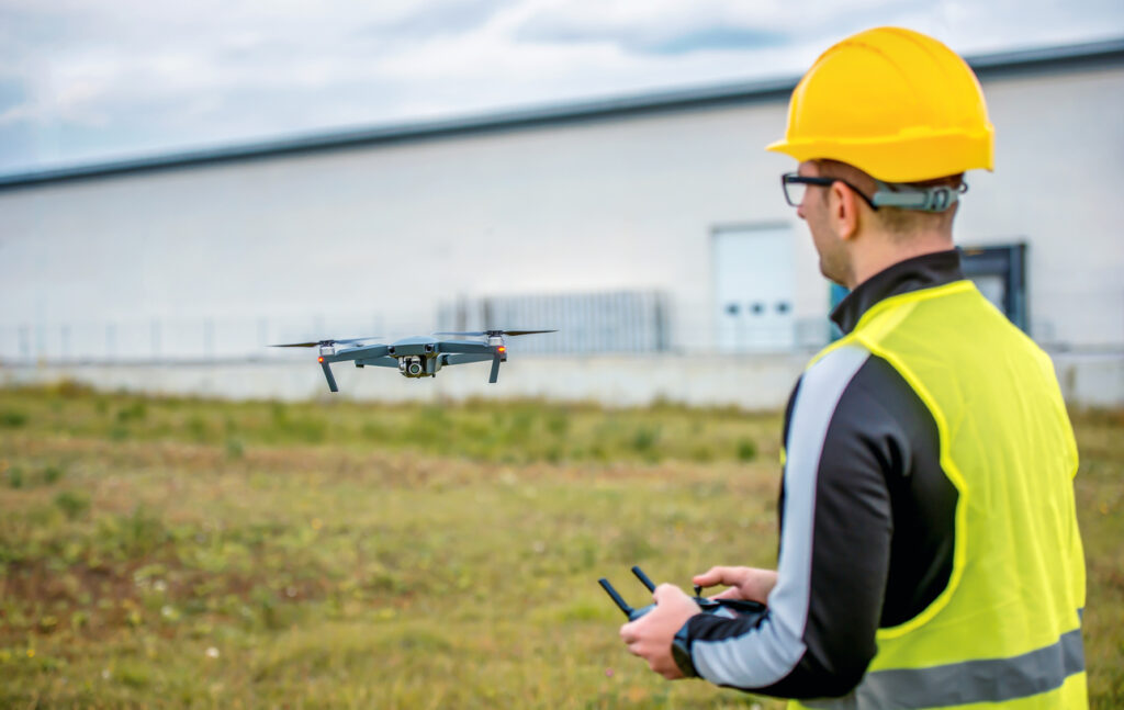 Man wearing a hard hat operating a drone using a remote control.