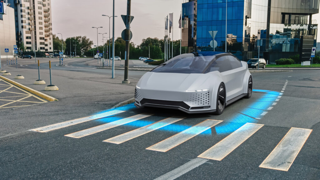 Silver autonomous car stopping before a crosswalk.