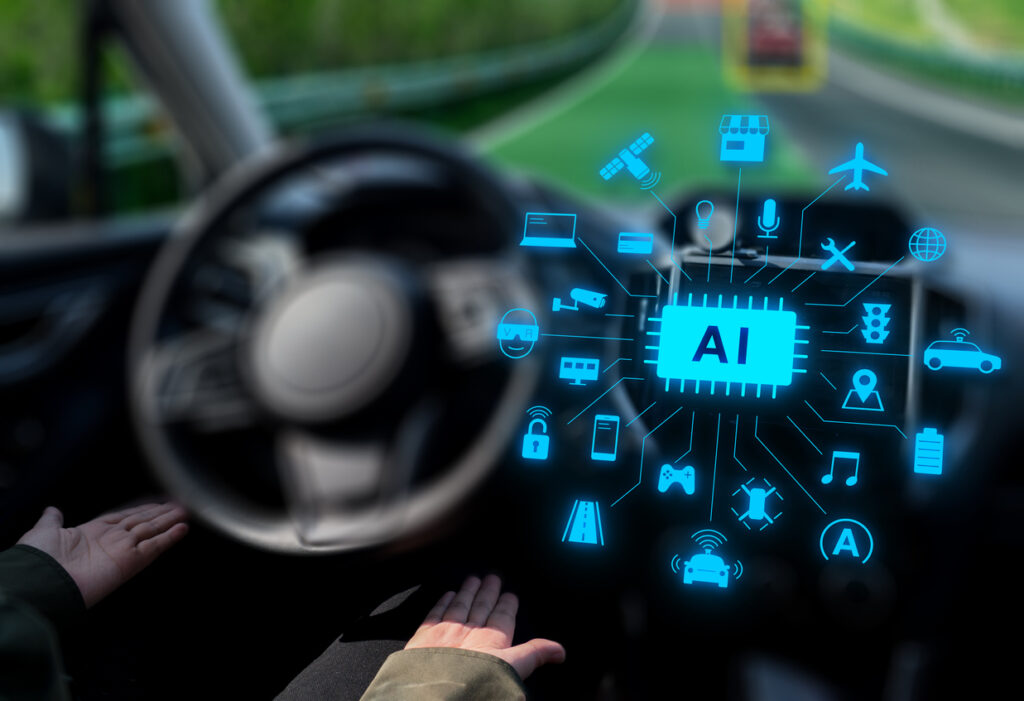 Hands below a vehicle’s steering wheel beside the artificial intelligence icons on a virtual screen.