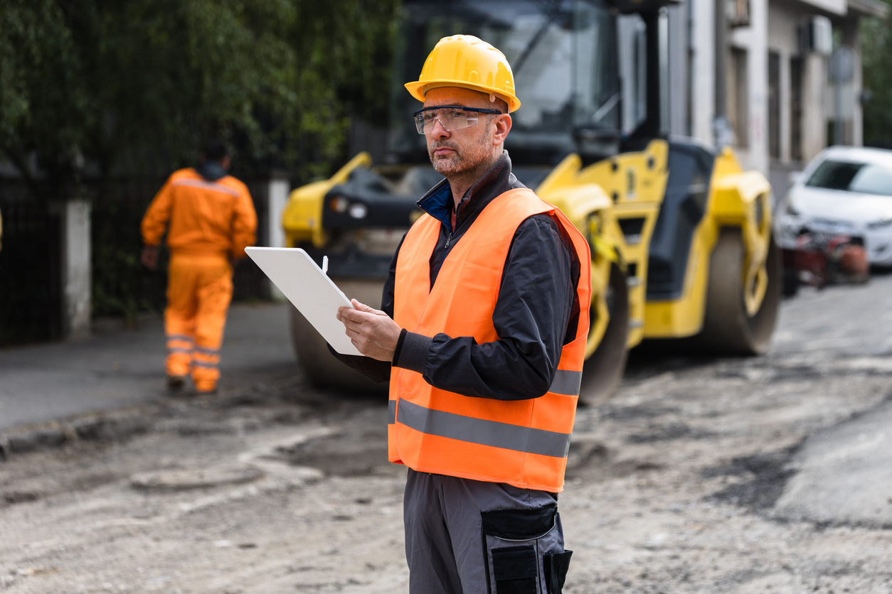 AI for Infrastructure Equity: Construction supervisor reviewing plans while overseeing roadwork in an urban area during the day