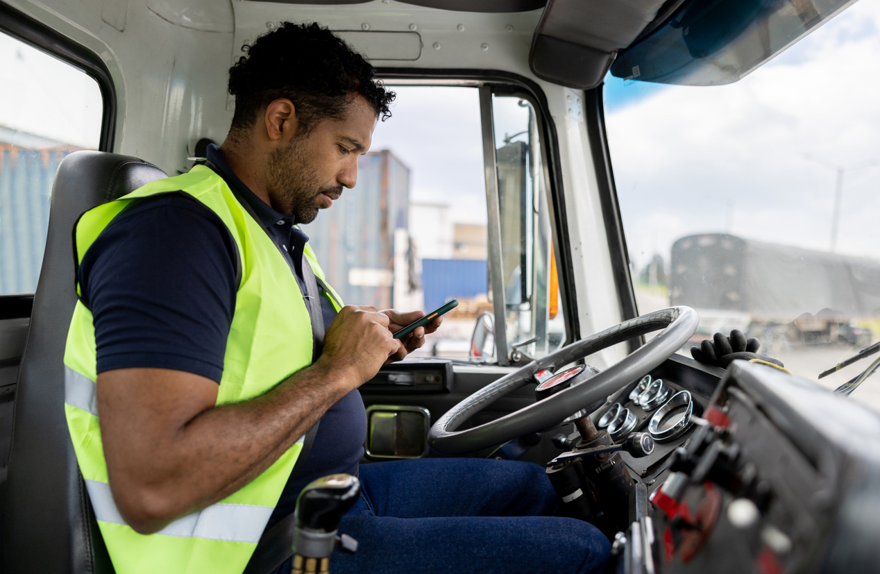 Roadway inspection methods - a male truck driver using his smartphone inside his truck.