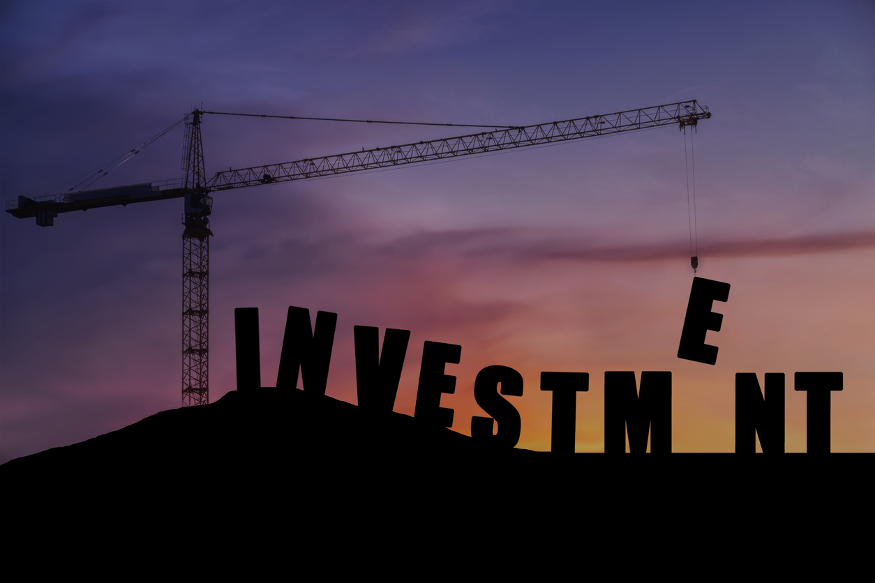 Crane lifting the letter “E” on the word “Investment” silhouette.