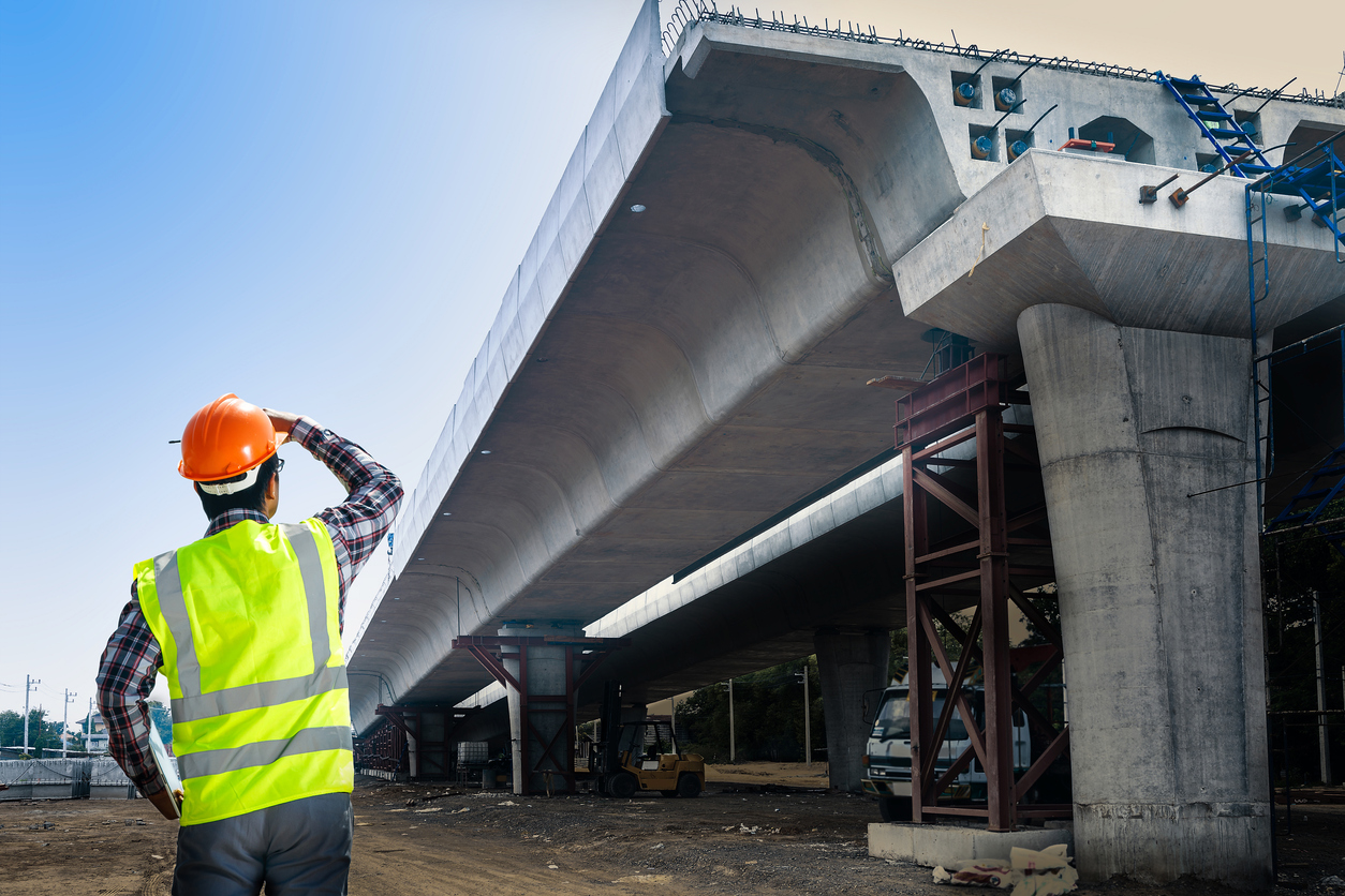 Underinvestment in infrastructure maintenance: Worker wearing an orange hard hat while looking at a bridge.