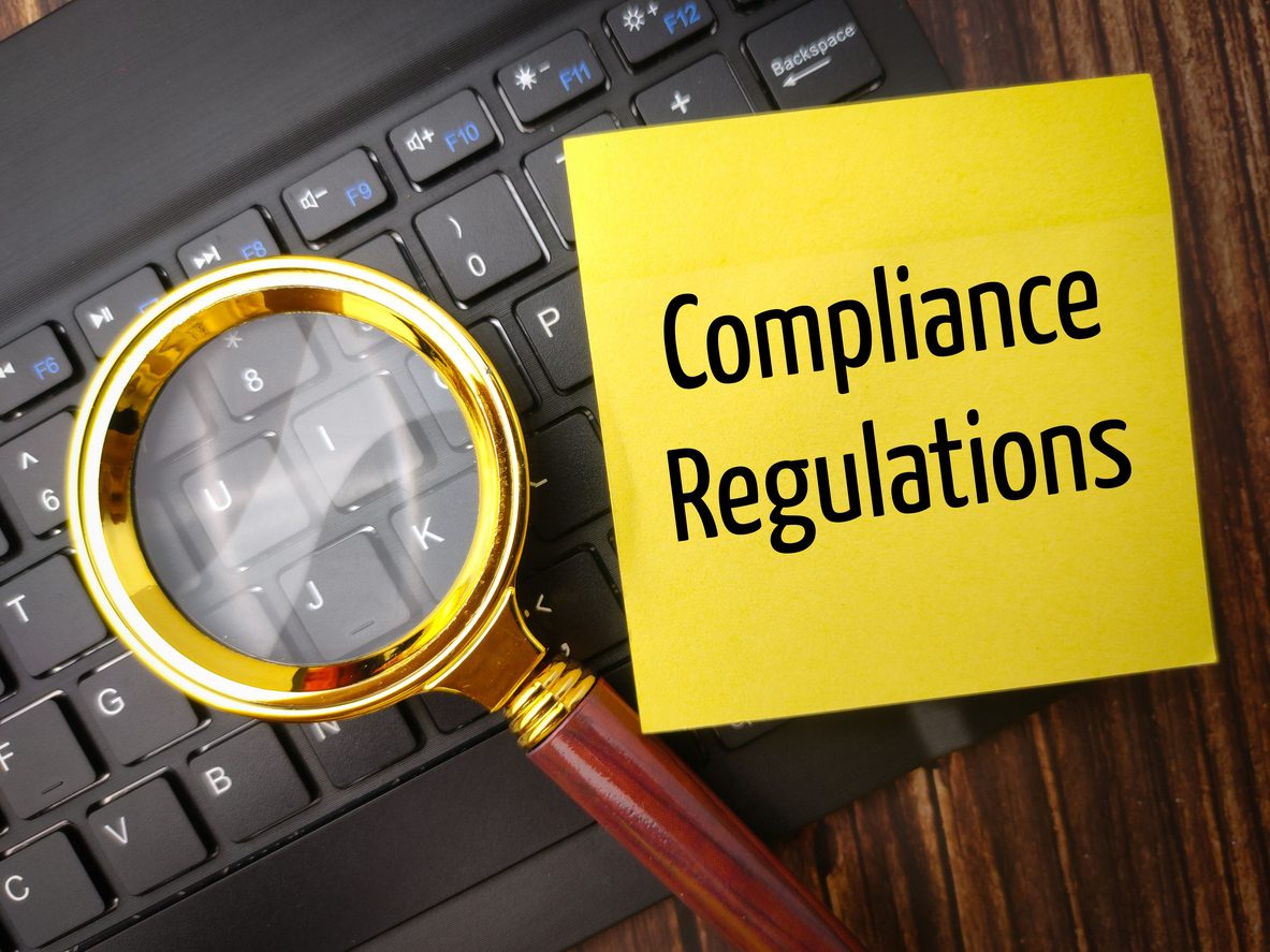 FHWA retroreflectivity compliance - a close-up shot of a magnifying glass and a paper with the text “compliance regulations” on top of a black keyboard.